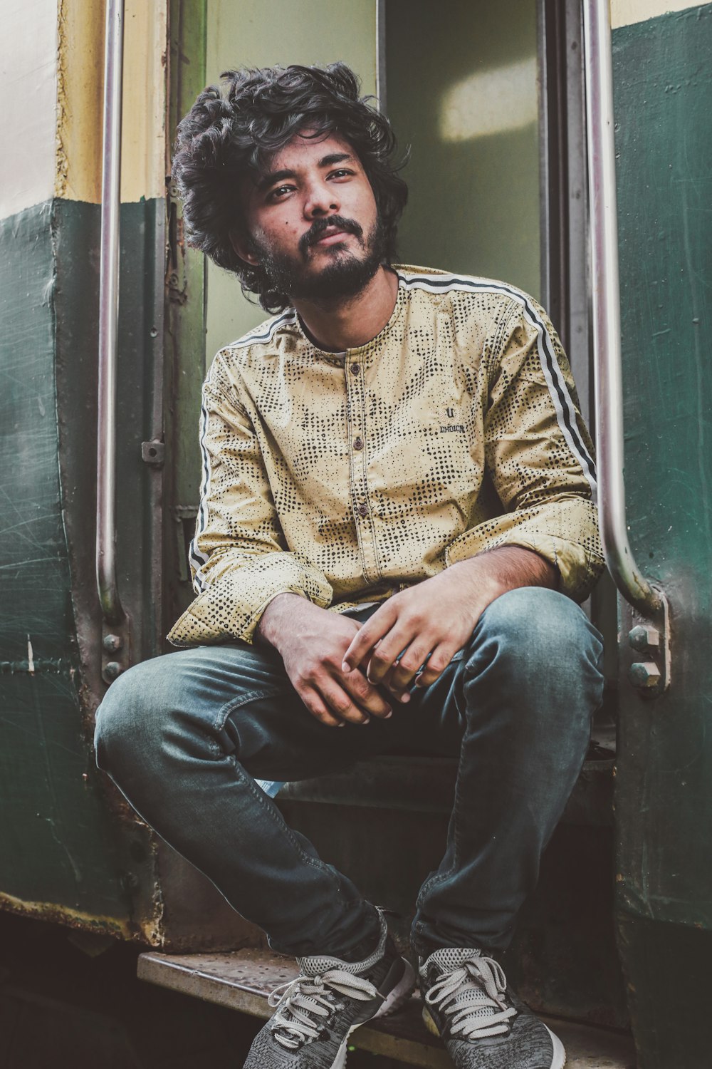 man in brown dress shirt and blue denim jeans sitting on black metal chair