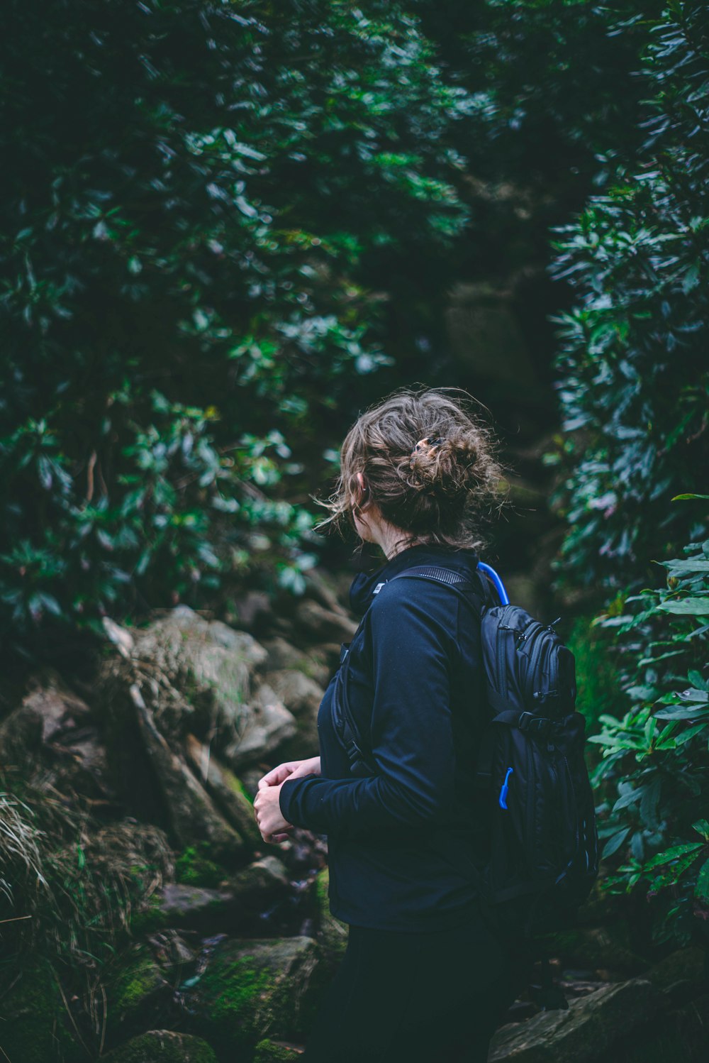 woman in blue jacket standing near green trees during daytime