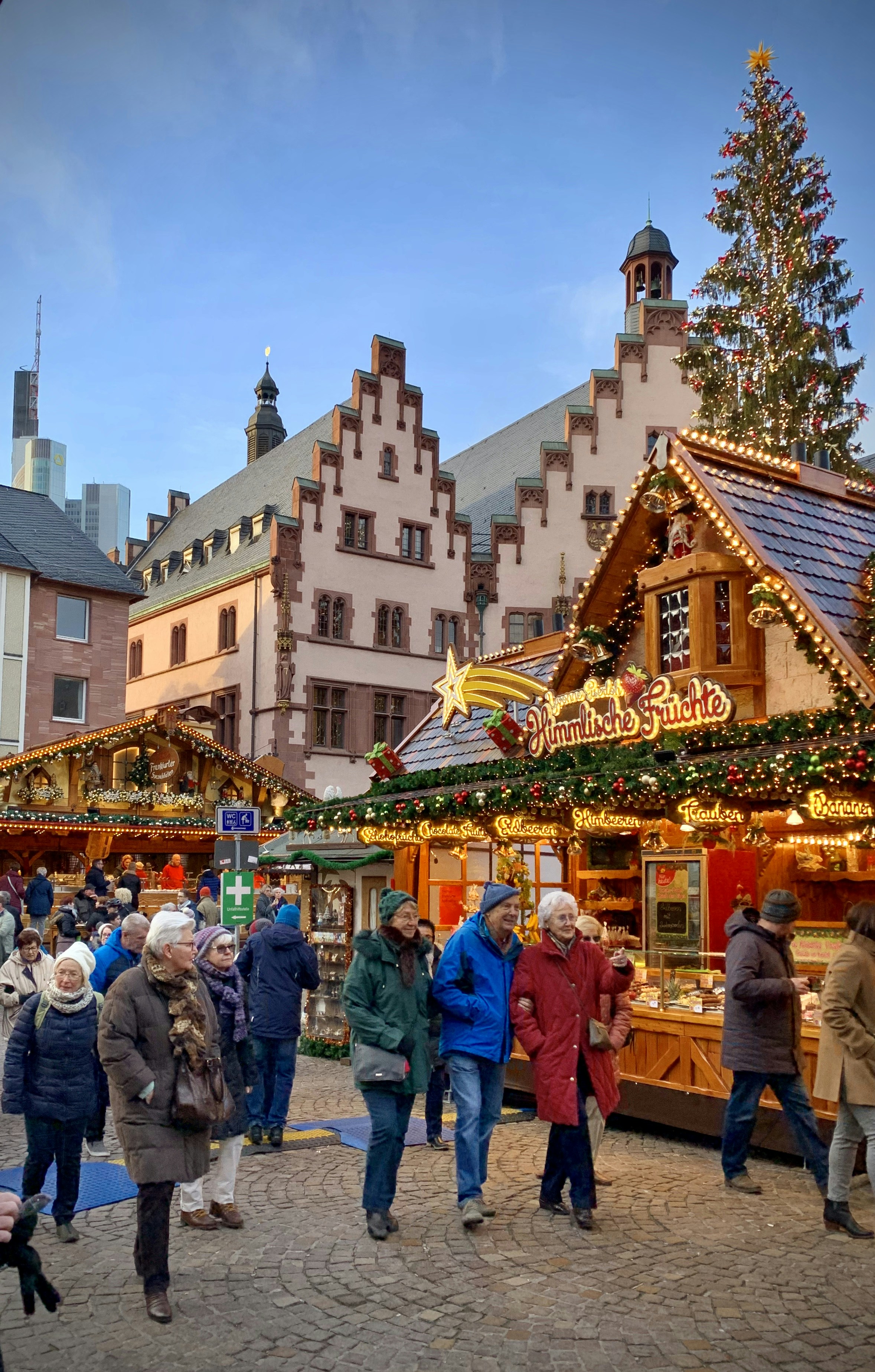 People browsing an outdoor Christmas market with stalls selling food and goods, set in a historic to