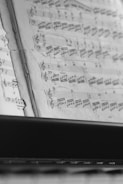 A close-up view of open sheet music showing musical notes and staff lines on pages. The focus is sharp on the notes, highlighting the intricate details of the musical composition. The image is captured in black and white, giving it a classic and timeless feel.