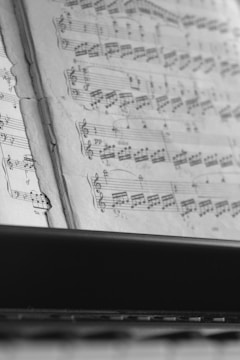 A close-up view of open sheet music showing musical notes and staff lines on pages. The focus is sharp on the notes, highlighting the intricate details of the musical composition. The image is captured in black and white, giving it a classic and timeless feel.