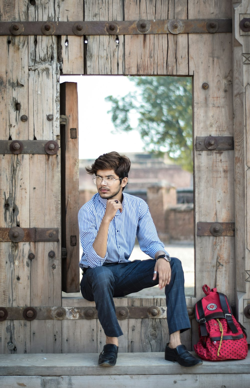 man in blue and white striped dress shirt and blue denim jeans sitting on brown wooden