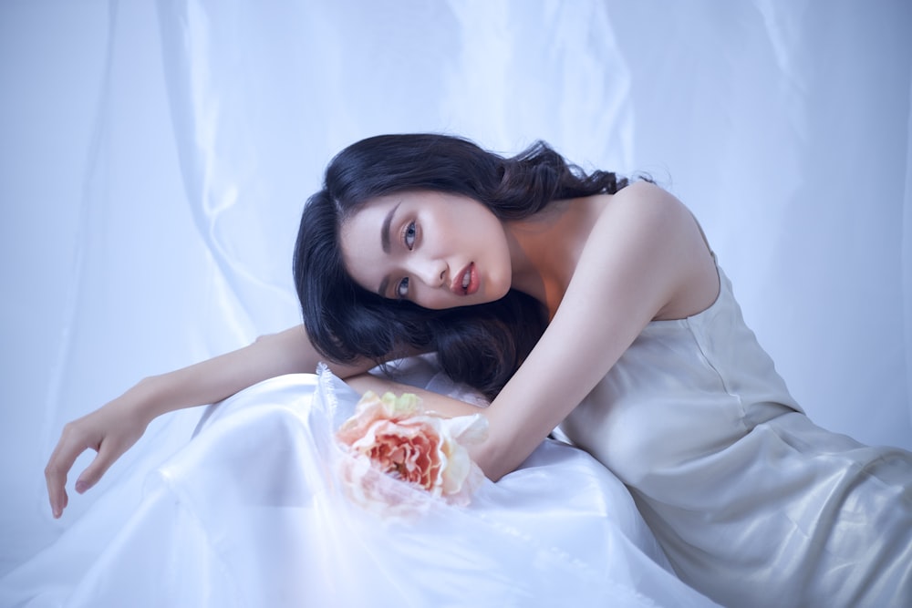 mujer con vestido blanco sin mangas acostado en cama blanca
