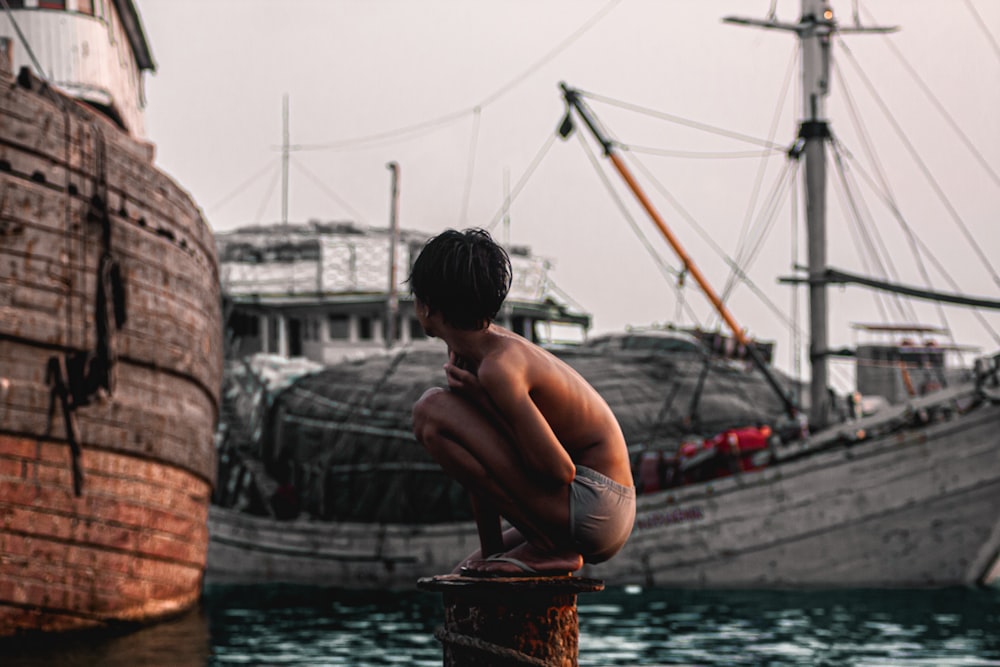 topless boy in brown shorts standing on brown wooden dock during daytime