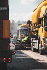 Heavy machinery working on a new road with workers coordinating in yellow safety gear.