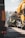A scene of road construction work with large yellow construction vehicles and workers in high-visibility clothing. Workers are seated on machinery in between the vehicles, which appear to be engaged in paving or maintenance work on a road.