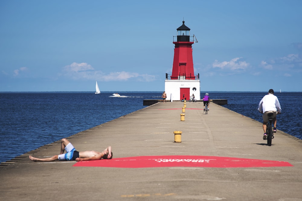 man in blue shorts lying on red concrete floor near white and red lighthouse during daytime