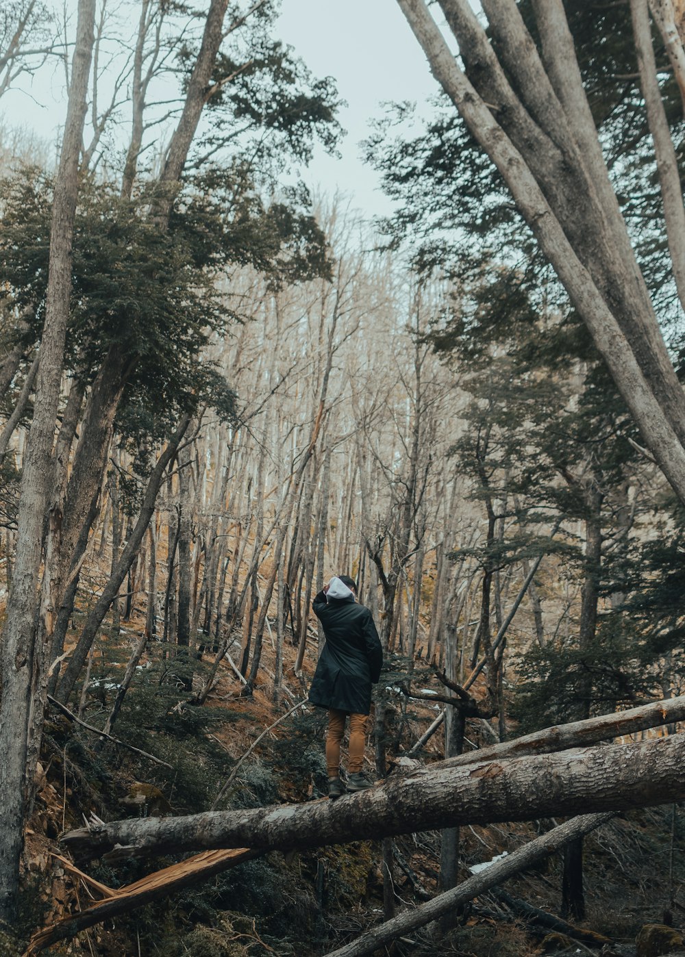 man in black jacket and blue denim jeans walking on brown wooden bridge surrounded by trees