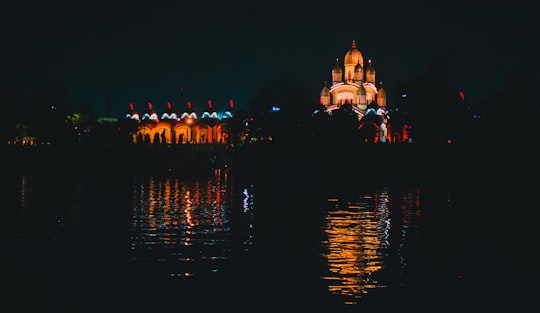 people walking on sidewalk near body of water during night time in Dakshineswar Kali Temple India