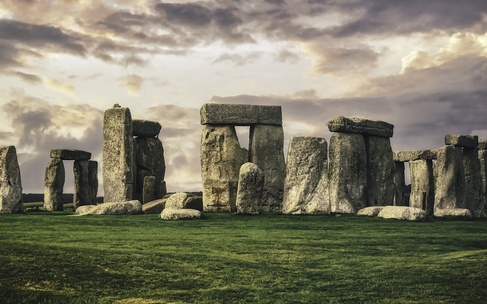 gray rock formation on green grass field under gray cloudy sky