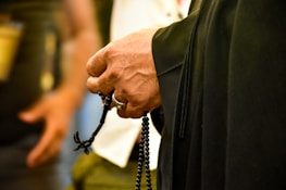 A close-up of hands gently holding a rosary with blurred stained glass in the background.