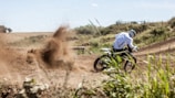 Close-up of a rider kicking up dirt as they power through a sharp turn under a cloudy sky.