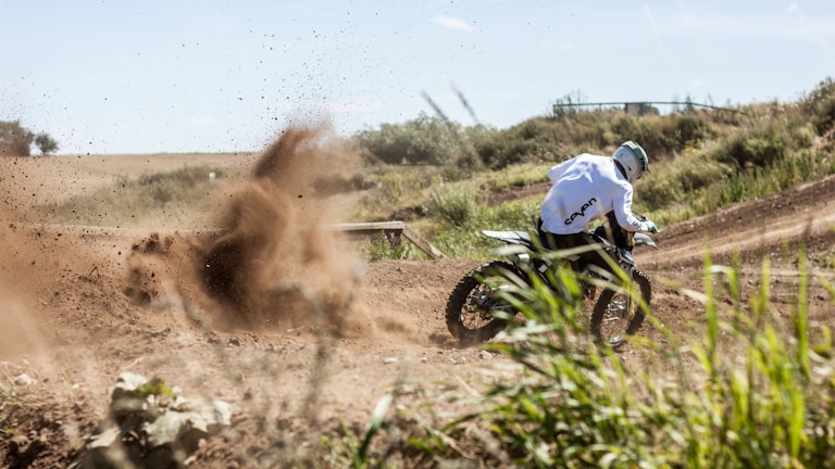 Close-up of a rider kicking up dirt as they power through a sharp turn under a cloudy sky.
