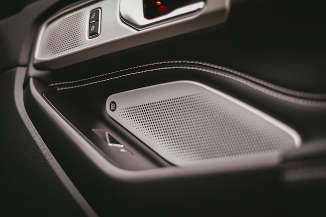 Close-up of a sleek car door panel with premium speaker upgrades and ambient blue lighting.