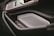 A close-up view of an interior car door panel featuring modern and sleek design elements. The panel includes a metallic speaker grille, an electronic lock control, and stitched leather detailing, suggesting luxury and technological advancement.