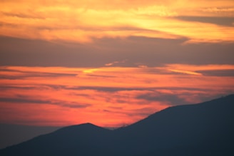 A painting capturing a fiery orange and pink sunset with soft hills beneath.