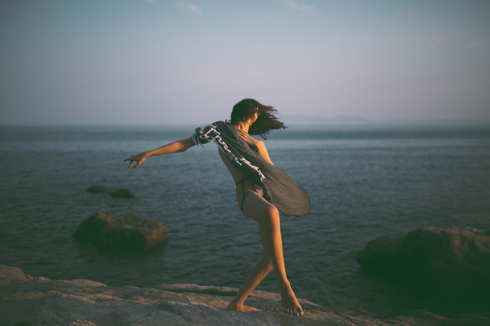 a woman standing on top of a rock near the ocean