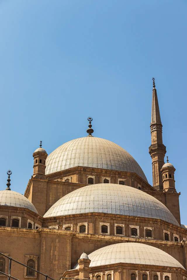 The Mosque of Muhammad Ali's silver domes and twin minarets rising above the Citadel's stone walls, with carved lion statues in the foreground.