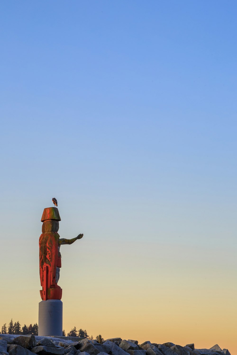 uomo in giacca nera e pantaloni marroni in piedi sulla roccia marrone sotto il cielo blu durante il giorno