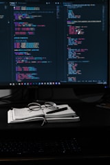 A cozy studio workspace with sketches, game design notes, and a glowing monitor showing a mysterious game scene.