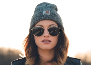 woman in black leather jacket wearing black sunglasses and gray knit cap