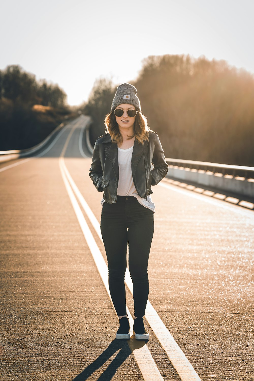 검은 재킷과 검은 바지를 입은 여자가 낮에 도로에 서 있다