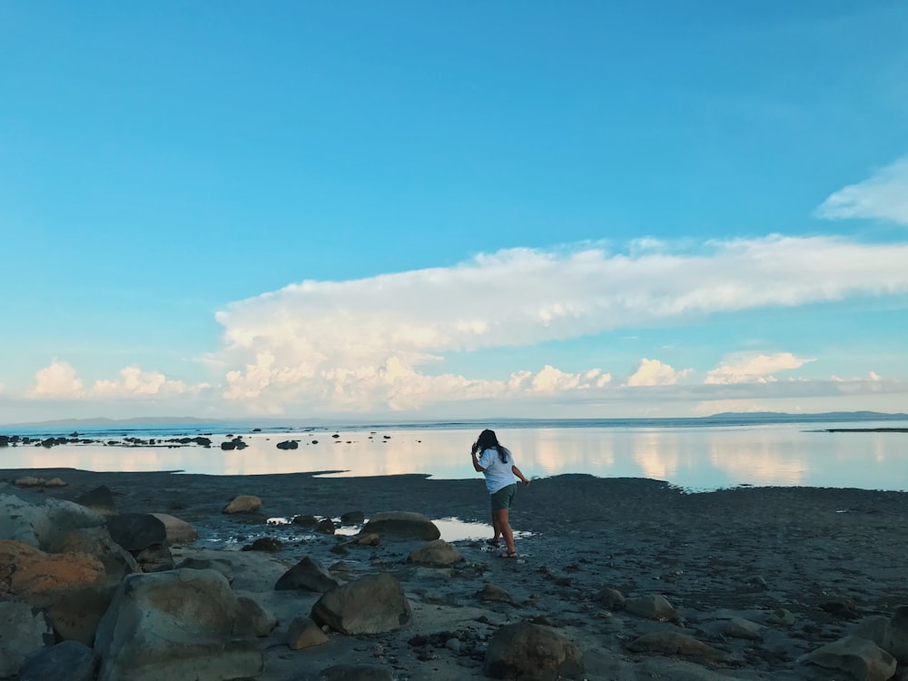 man in white t-shirt and black shorts standing on rocky shore during daytime