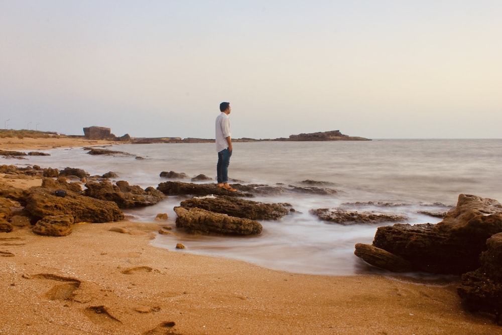man in white shirt standing on brown sand near body of water during daytime