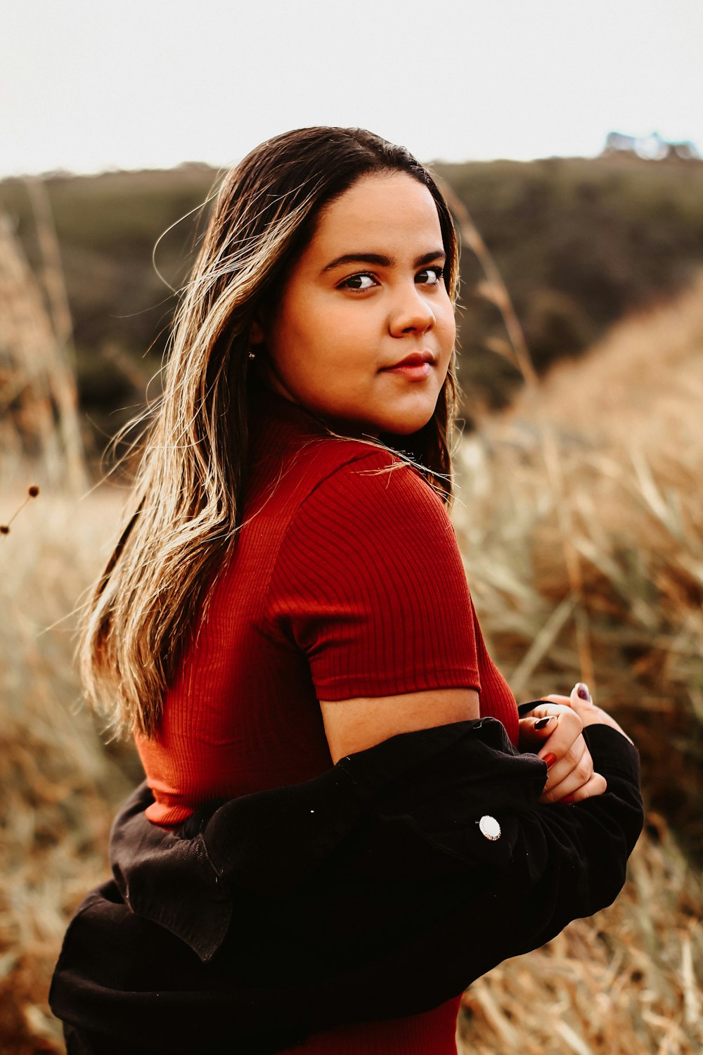 woman in red long sleeve shirt and black skirt sitting on brown grass field during daytime