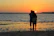 A couple embracing on a quiet Oahu beach with vibrant sunset colors behind them.