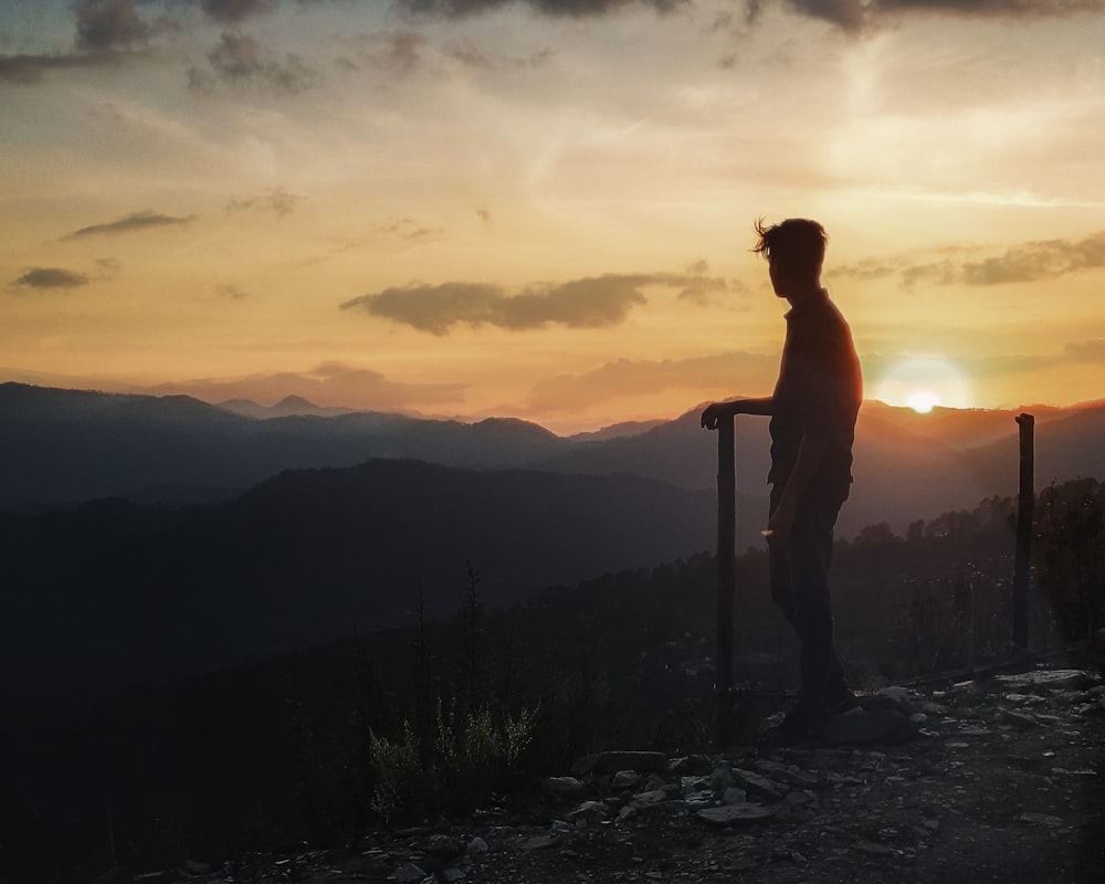 woman in red long sleeve shirt standing on rock during sunset