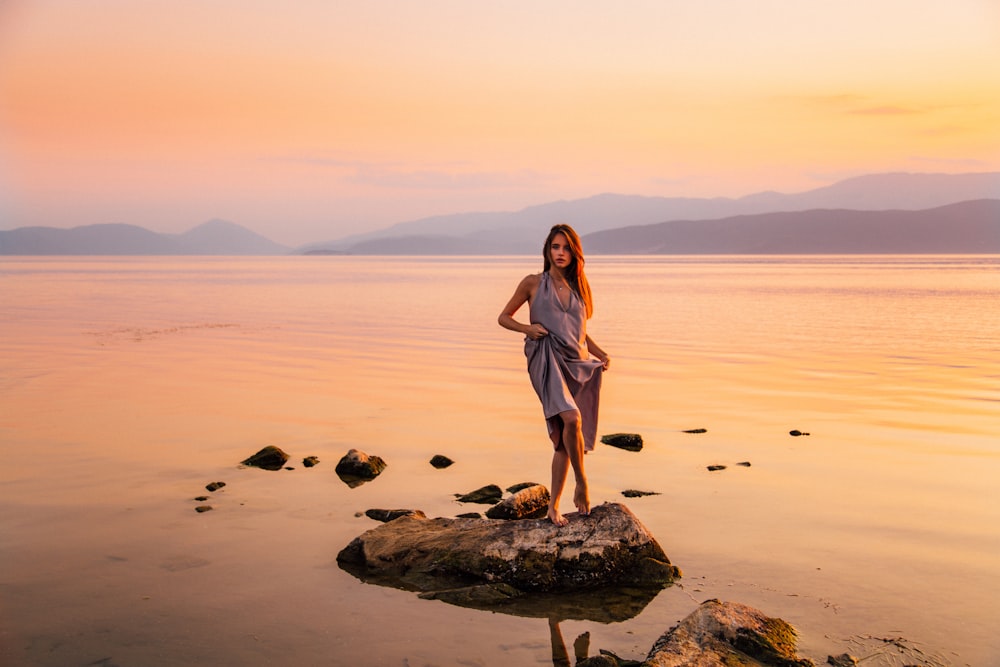 woman in white dress standing on rock near body of water during daytime