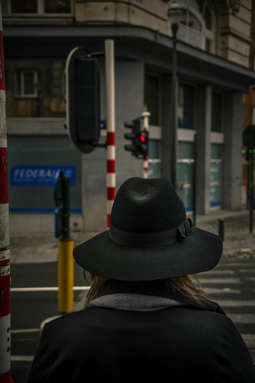 woman in black hat and brown coat standing near pedestrian lane during daytime