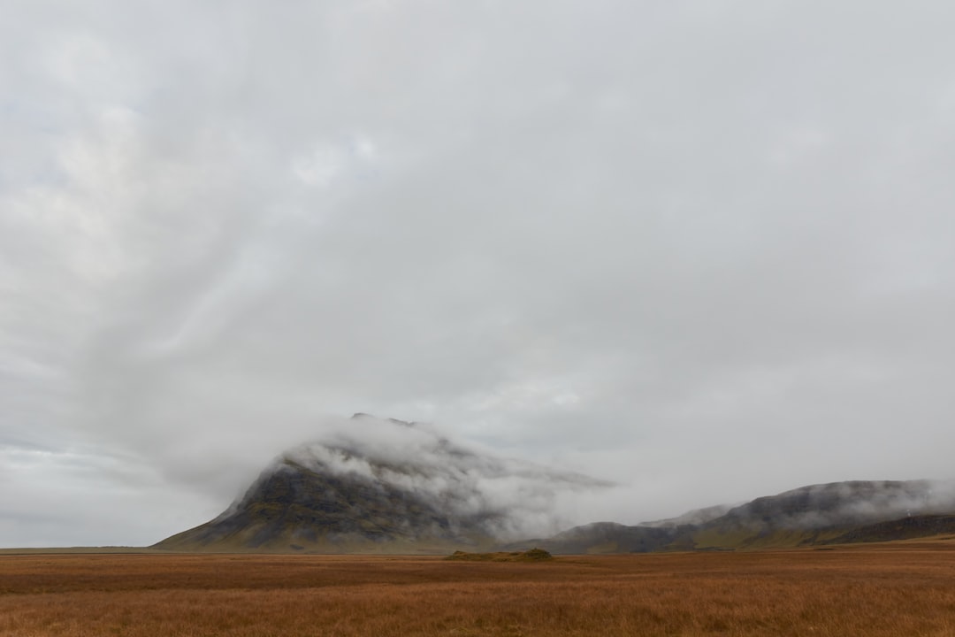 brown field near mountain under white clouds during daytime