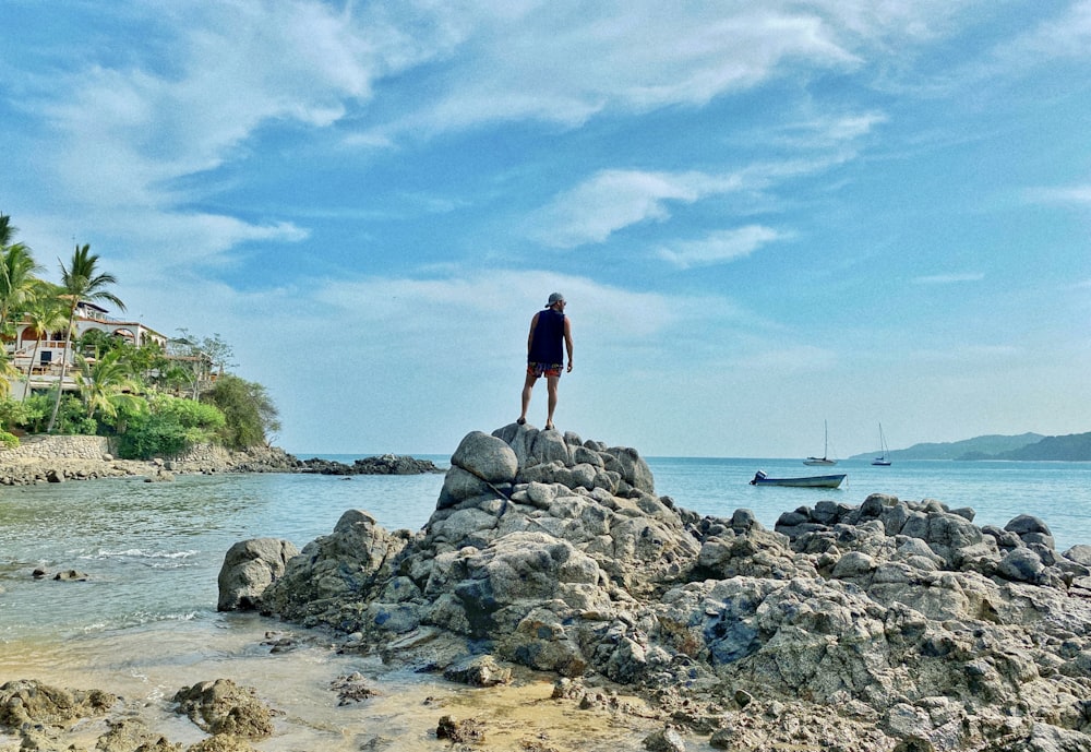 woman in black dress standing on gray rock formation near body of water during daytime