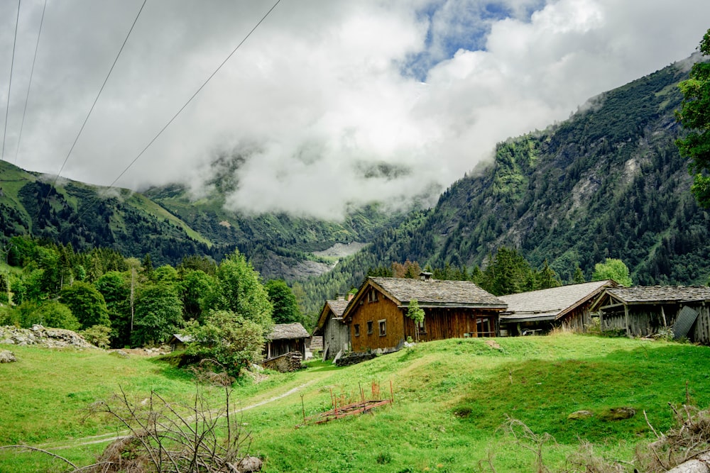 昼間は白い雲の下、山の近くの緑の芝生の上の茶色の木造家屋