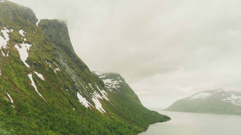 green and black mountain beside body of water under white cloudy sky during daytime