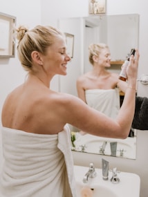 woman in white towel appyling skincare mist to her face.