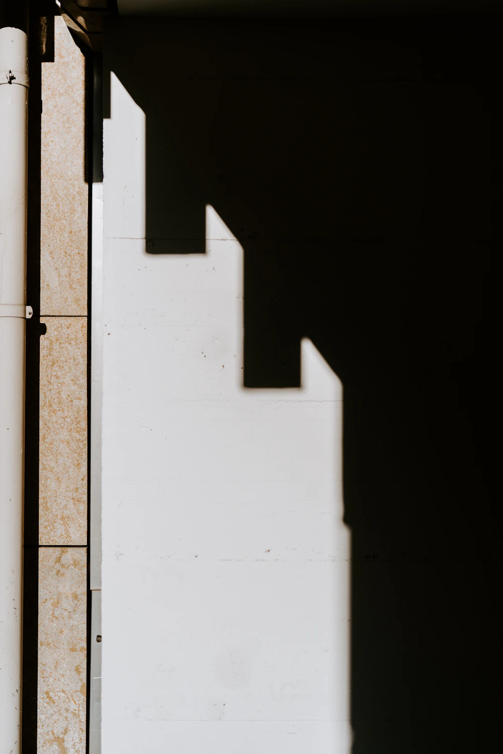 A white concrete wall split by a sharp, stepped shadow under a clear sky
