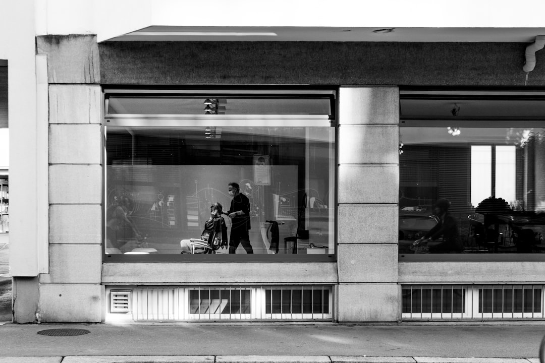 grayscale photo of people sitting on bench in front of building