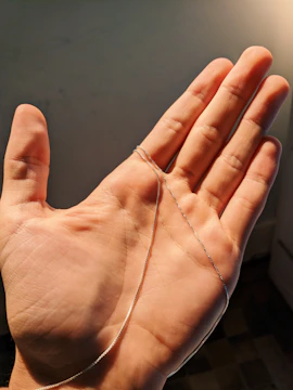 Hands threading a silver chain with tiny charms in a sunlit studio.