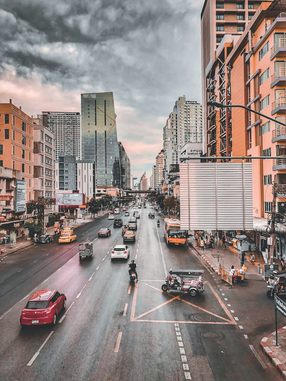 cars on road between high rise buildings under gray clouds during daytime