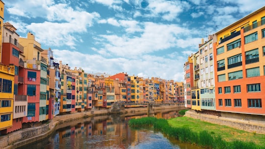 brown and white concrete buildings near river under white clouds and blue sky during daytime in Onyar River Spain