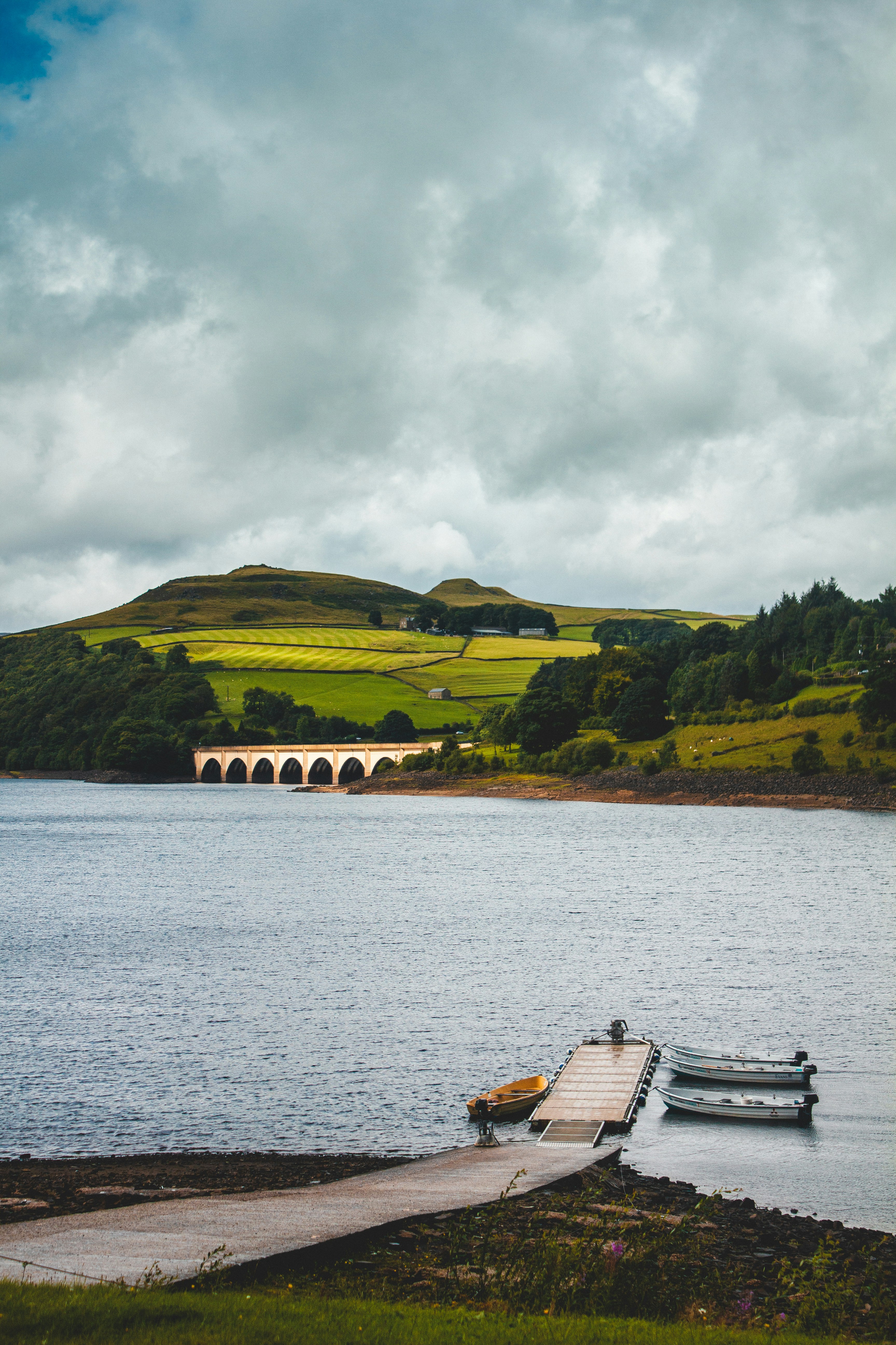 brown wooden boat on river near green mountain under white clouds during daytime