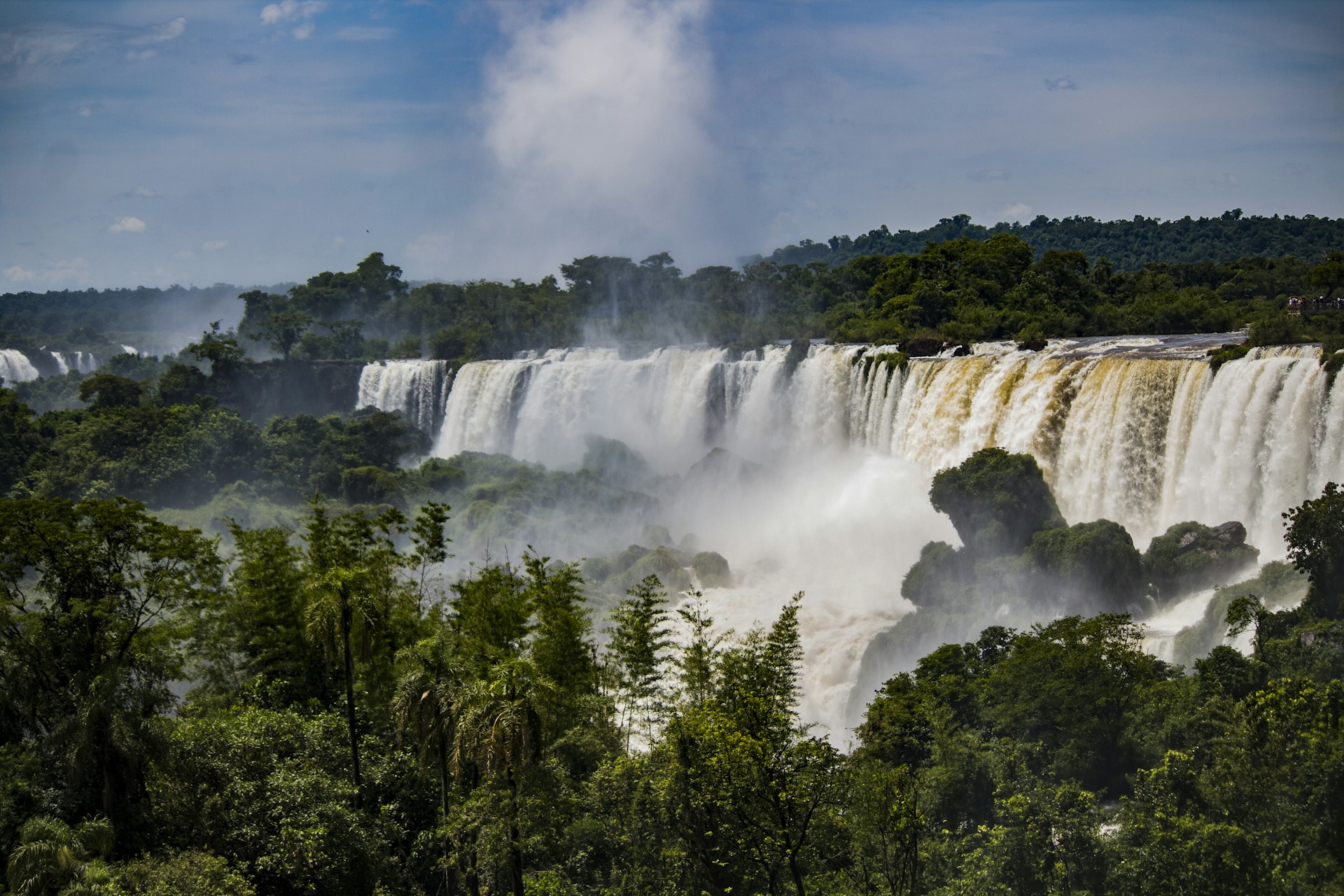 waterfalls in the middle of green trees under blue sky and white clouds during daytime
