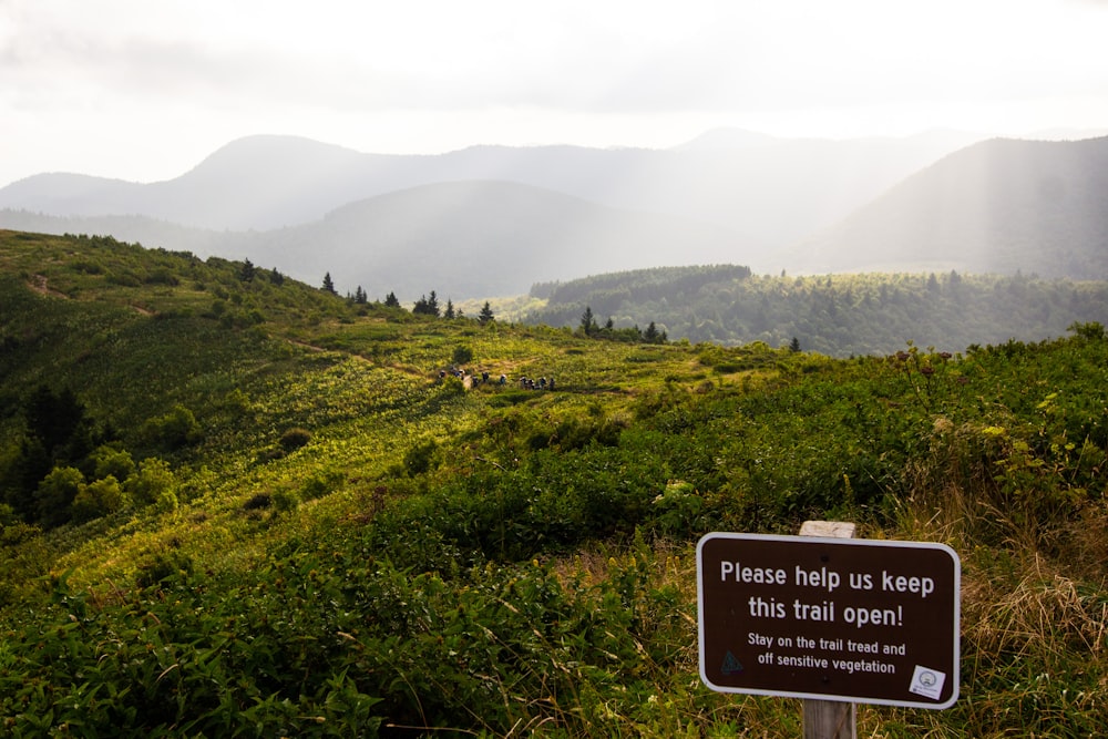 a sign on the side of a hill that says please help us keep this trail