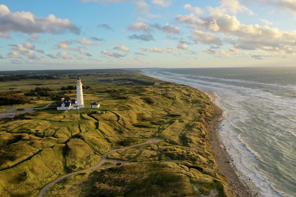 white lighthouse on brown rocky shore under blue and white sunny cloudy sky during daytime