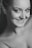 A close-up black and white portrait of a smiling person with light skin. The person is looking directly at the camera, conveying a sense of warmth and confidence. The image focuses on facial features, with particular emphasis on the eyes and smile.