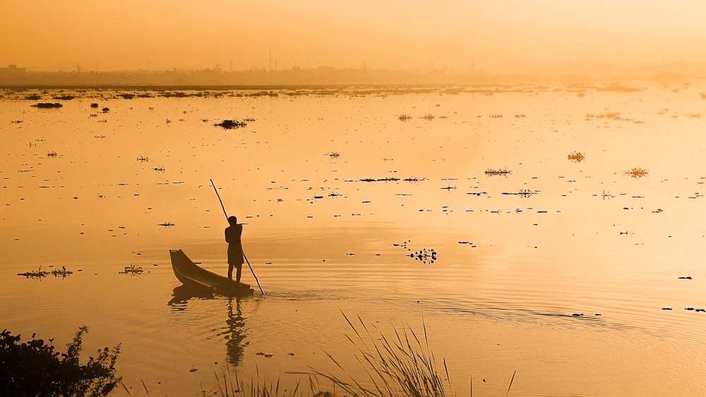 silhouette of man riding on boat on water during sunset