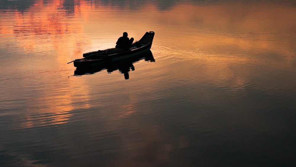 silhouette of 2 people riding on boat on calm water during sunset